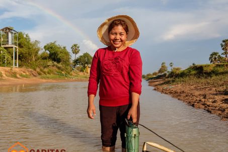 Phany adjusts her water pump in the canal outside her home in Western Cambodia