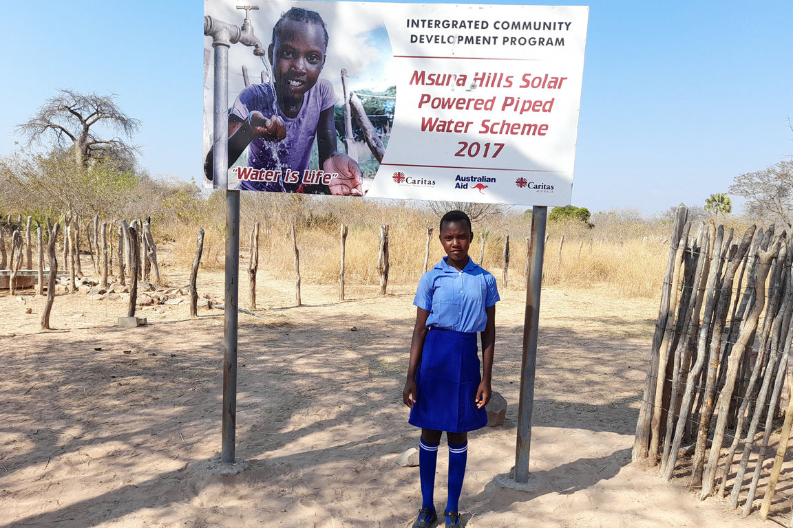 Thandolowayo standing underneath Integrated Community Development Program sign in Zimbabwe