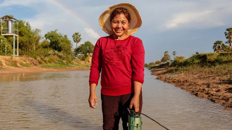 Phany adjusts her water pump in the canal outside her home in Western Cambodia